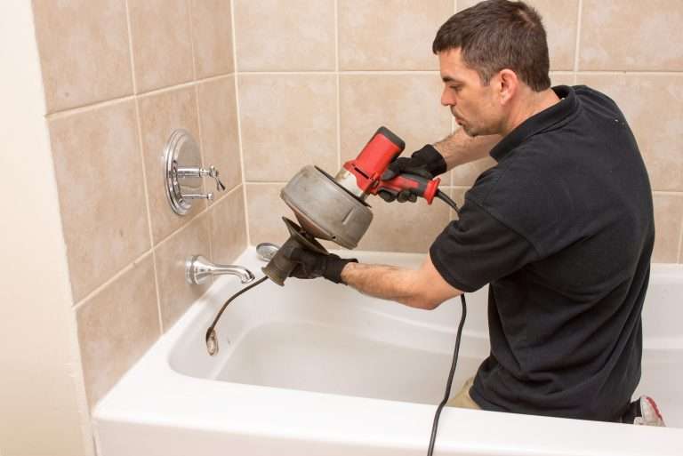Plumber unclogging a tub drain with an electric rooter